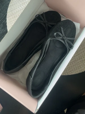 Svarta spetsballerinaskor med rosett - Snygga svarta ballerinaskor med spetsdetaljer och liten rosett framtill. Skorna har rundad tå och sidor i genombruten spets som ger en trendig look. Perfekta för dig som vill ha en feminin och stilren sko till vardagsoutfiten.