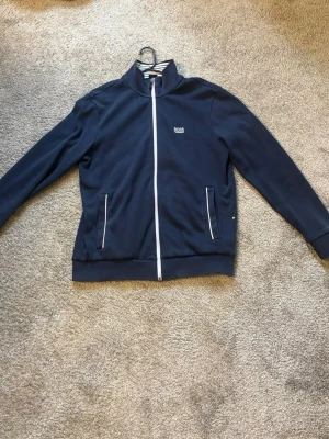 Huga Boss tröja - Säljer en mörkblå zip-up från Hugo Boss. Väldigt stilren och passar till både vardag och lite mer uppklätt. Tröjan är i bra skick, inga större slitningar. Skön passform och bra kvalitet som håller länge. Dragkedja framtill och fickor på sidorna.