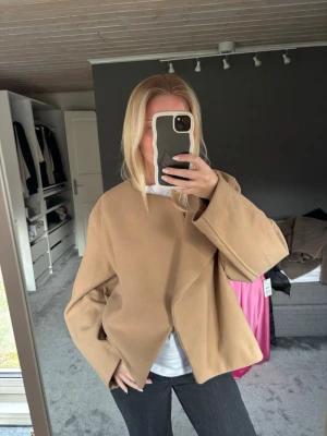 Beige oversized kappa - Säljer en beige oversized kappa med minimalistisk design och vida ärmar. Kappan har en öppen front utan synliga knappar 