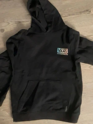 Svart hoodie från Vans med tryck - Svart hoodie från Vans. Stor färgglad 'Off The Wall Vans'-grafik på ryggen. Mjuk bomullsmix, huva och stor magficka framtill. Hoodien är i storlek L i barnstorlek så den är som en XS 💕