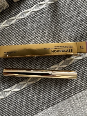 Hourglass Volumizing Glossy Stick - Snyggt läppglans i pennformat från Hourglass i nyansen Slip 125. Kommer i en lyxig, guldig hylsa och ger glansiga, fylliga läppar. Perfekt för dig som vill ha ett glossigt resultat med volym.
