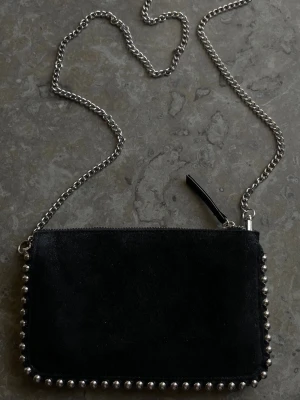 Svart axelväska med nitar och kedja - Säljer en liten svart väska med kedja. Perfekt när man bara vill ha med det viktigaste – mobil, kort osv.  Använd men i bra skick.
