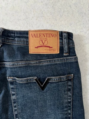 Valentino Jeans - Snygga mörkblå jeans från Valentino med klassisk femficksmodell och rak passform. Jeansen har en tydlig V-detalj på bakfickan och ett brunt läderpatch med logga i midjan. Tillverkade i slitstark denim som ger en tidlös look.