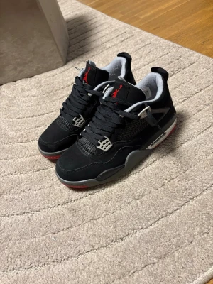 Air Jordan 4 Retro bred Black/red  - Snygga Air Jordan 4 Retro sneakers i svart mocka med röda och grå detaljer. Skorna har den klassiska Jumpman-loggan på plösen, meshpaneler på sidorna och plastdetaljer vid snörningen. Använda cirka 5 gånger 