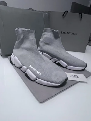 Grå Balenciaga Speed Trainer sneakers - Grå Balenciaga Speed Trainer sneakers med stickad ovandel i textil och vit, chunky sula med svarta detaljer. Strumpliknande passform och Balenciaga-logga på sidan. Superlätta och flexibla för en modern streetwear-look.
