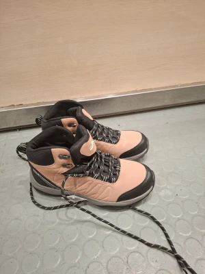 Beige och svarta kängor från crivit  - Snygga kängor från  i beige och svart med högt skaft och vadderad insida. Skorna har grova svarta och vita snören, metallhål för snörning och slitstark sula. Perfekta för dig som vill ha både stil och funktion under höst och vinter.