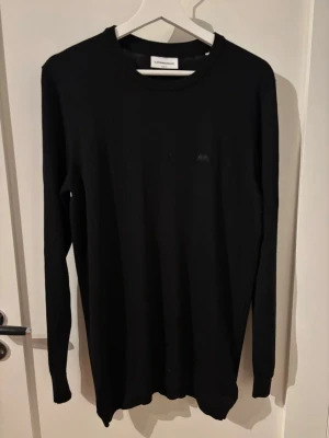 Svart stickad tröja J.Lindeberg - Snygg svart stickad tröja från J.Lindeberg med rund halsringning och diskret logga på bröstet. Tröjan har lång ärm och är tillverkad i ett mjukt, tunt material som passar perfekt till lager på lager. Enkel och stilren design. Köpt på jeansbolaget för 599kr. Använd Max 3 gånger.