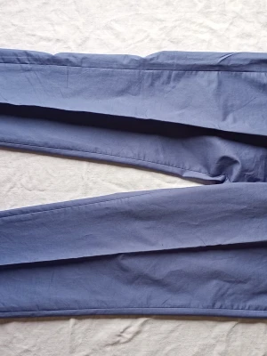 Blå kostym med tvåknäppt kavaj - Snygg blå kostym med matchande byxor och tvåknäppt kavaj. Klassisk passform med fickor fram och slät finish. Perfekt för dig som vill ha en stilren look till student eller bal. Materialet känns lätt och passar bra till vår och sommar.