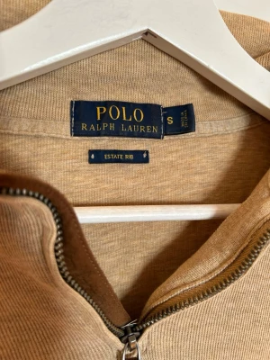 Beige ziptröja Polo Ralph Lauren - Snygg beige ziptröja från Polo Ralph Lauren i ribbad bomull. Klassisk halvzip med liten broderad logga på bröstet. Perfekt för dig som gillar stilrena och tidlösa plagg med premiumkänsla. Pris kan diskuteras!