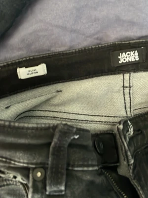 Svarta slim jeans från Jack & Jones - Snygga svarta slim fit jeans från Jack & Jones med klassisk femficksmodell och diskreta slitningar. Jeansen har smal passform och är tillverkade i ett stretchigt material för extra komfort. Perfekta för en trendig och avslappnad stil.