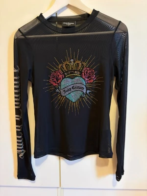 Svart mesh topp Juicy Couture - Snygg svart mesh topp från Juicy Couture med lång ärm och coolt tryck framtill med hjärta, rosor och krona i färgglada stenar. Texten 'Juicy Couture' syns på ärmen i glittriga stenar. Perfekt statement-plagg för dig som vill sticka ut. Jättefint skick. Aldrig använd.
