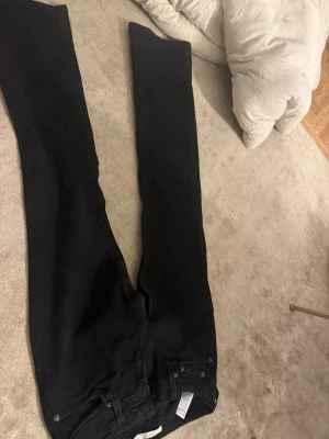 Svarta bootcut jeans Superlow 26 - Säljer ett par svarta bootcut jeans från Superlow Boot i storlek 26. Jeansen har klassisk femficksdesign, bälteshällor och knappgylf. Perfekta för dig som gillar en tidlös och avslappnad look.