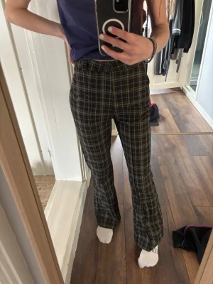 Rutig bootcut byxa i grönt och svart - Snygga bootcut-byxor med rutigt mönster i grönt, svart och vitt. Hög midja och klassisk passform som sitter bekvämt. HM storlek S, aldrig använt. 