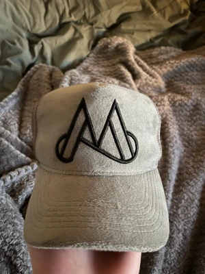 Beige keps från Maggiore - Säljer en beige keps från Maggiore med svart broderad logga framtill. Kepsen har klassisk böjd skärm och justerbar snapback baktill. Tillverkad i mjukt tyg som ger en avslappnad och stilren look. Perfekt accessoar för att lyfta din outfit.