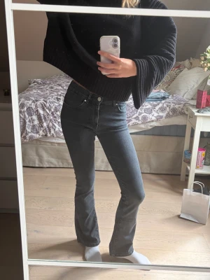 Svarta bootcut jeans med hög midja - Snygga svarta bootcut jeans med hög midja och klassisk femficksdesign. Jeansen har en smal passform upptill och lätt utsvängda ben. Perfekta för dig som vill ha en modern och stilren look. Materialet är denim med stretch för extra komfort.