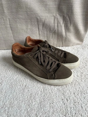 Mörkbruna sneakers från Strömberg - Snygga mörkbruna sneakers från Storksak i mocka med vita sulor och bruna skosnören. Insidan är fodrad i brunt läder för extra komfort. Klassisk låg modell som passar till det mesta och ger en clean look. litet hål som syns på sista bilden, inget stort men om man vill så går ju allting att laga. 