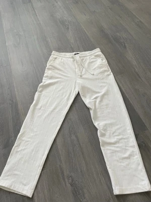 Vita linnebyxor  - Snygga vita linnebyxor med avslappnad passform och elastisk midja med dragsko. Byxorna har raka ben och sidofickor, perfekta för en chill och stilren look. Materialet är luftigt linne som passar perfekt till varmare dagar.
