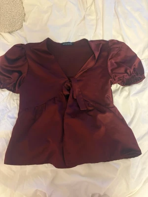 Vinröd satinblus med puffärm Missay - Snygg vinröd blus i glansigt satintyg från Missay. Modellen har puffärmar med resår, knytning framtill och v-ringning. Aldrig använt och inga skador❣️ 