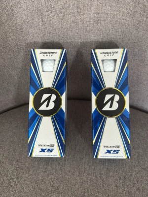 Bridgestone Tour B XS golfbollar - Två förpackningar Bridgestone Tour B XS golfbollar med blå, vit och gul design. Perfekta för dig som vill ha högpresterande golfbollar till spelet. Snygg förpackning med tydlig logga och fönster som visar bollarna.