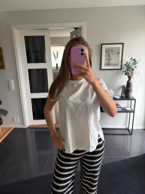 Vit t-shirt med knappar i ryggen - Vit t-shirt i bomull med rund hals och korta ärmar. Baksidan har en rad stora dekorativa knappar som ger en unik twist till den klassiska modellen. Passformen är loose och tyget känns luftigt och skönt.