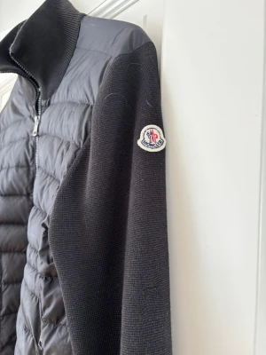Svart cardiganjacka från Moncler - Snygg svart cardiganjacka från Moncler! Storlek M i herr, säljer åt min storebror:) dragkedjan är lagad hos skräddare så den är i toppenskick! Finns ett litet hål i en ficka men går enkelt att laga;)