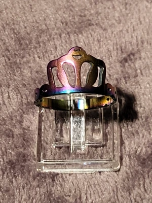 Regnbågsfärgad kronring i metall - Cool ring i metall med regnbågsskimrande yta och ett utstansat kronmotiv. Ringen har en unik form som sticker ut och passar perfekt för dig som vill ha något annorlunda. Märke saknas.