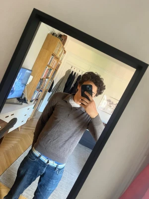 Brun långärmad piké tröja från Uniqlo - Säljer en stilren brun långärmad tröja från Uniqlo med krage och tre knappar framtill. Tröjan är i mjukt material och har en klassisk passform som funkar till många olika looks. Perfekt för dig som gillar enkel och clean stil.