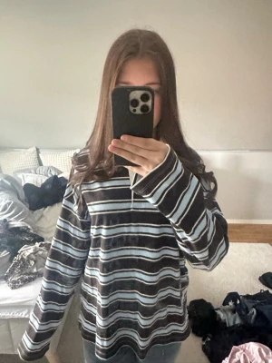 Randig rugbytröja med krage - Säljer en oversized rugbytröja med bruna, vita och ljusblå ränder. Tröjan har lång ärm, vit krage och knappar vid halsen. Perfekt för dig som gillar retrovibbar och avslappnad stil.