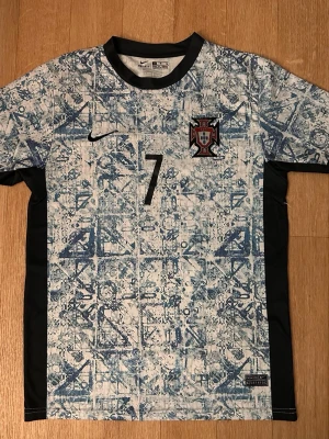Portugal Nike fotbollströja blå/vit - Säljer en Portugal fotbollströja från Nike i blått och vitt med grafiskt mönster. Tröjan har svart krage, svarta sidopaneler och nummer 7 på bröstet. Portugal-emblemet och Nike-loggan finns på framsidan. Tillverkad i Dri-FIT material för bra ventilation. M men passar även för S 