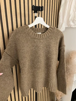Brun oversized stickad tröja - Mysig brun stickad tröja i oversized modell med rund halsringning och breda ribbade muddar. Tröjan har en avslappnad passform och är tillverkad i ett mjukt, grovt garn som ger en varm känsla. Perfekt för lager på lager under kyliga dagar.