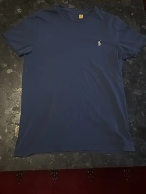 Blå polo ralph lauren t shirt - Blå polo ralph lauren t shirt, storlek s, har en defekt vid nedre magen där det är ett litet hål