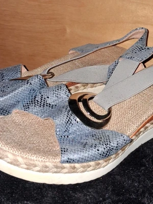Sandaler  - Sandaler med blått ormmönstrat band, elastiska grå remmar och dekorativa metallringar. Sulan är i flätad jute-look med vit undersida. 