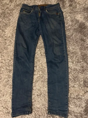 Mörkblå  jeans sand Copenhagen  - Säljer ett par mörkblå slim fit jeans med klassisk femficksdesign och dragkedjegylf. Jeansen har en snygg tvätt och smal passform som sitter tajt längs benen. Materialet är denim i bomull med lite stretch för extra komfort.