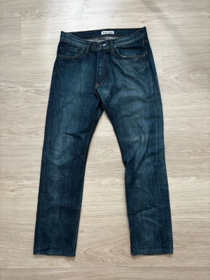 Mörkblå raka jeans från Acne Jeans - Snygga mörkblå jeans från Acne Studios med klassisk rak passform och fem fickor. Jeansen har subtila slitningar och kontrastsömmar för en cool look. Tillverkade i kraftigt denimtyg som ger en tidlös känsla. Storleken är 31/32 på lappen men de passar mera som 30/31