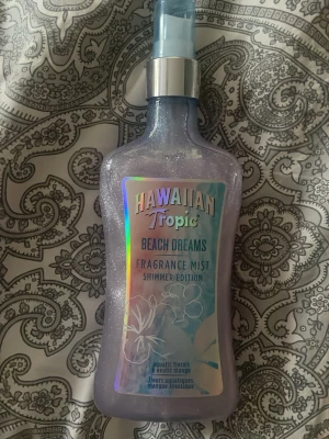 Hawaiian Tropic Beach Dreams Mist - HELT OANVÄND!!! Fräsch doftmist från Hawaiian Tropic i varianten Beach Dreams Shimmer Edition. Flaskan är skimrande ljuslila med holografisk etikett och spraymunstycke i blått och silver. Doften har inslag av akvatiska och exotiska blommor. Perfekt för dig som vill ha en lätt och glittrig parfym.