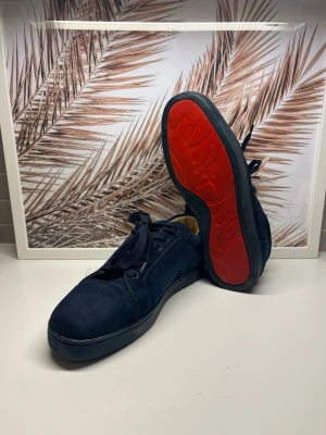 Marinblåa Christian Louboutin - Snygga blåa sneakers från Christian Louboutin med ikonisk röd sula. Skorna har lågt skaft, marinblåa snören och är tillverkade i mocka. Perfekta för dig som vill sticka ut med exklusiv design och coola detaljer. Skorna är i storlek 43