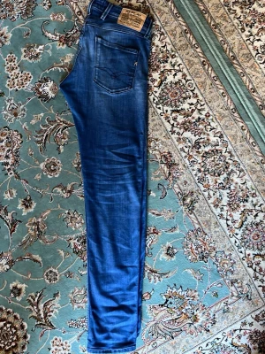 Blå jeans från Replay - Säljer ett par blå jeans från Replay med klassisk femficksmodell . Jeansen har raka ben och tydliga sömmar på bakfickorna. Tillverkade i mjukt denimtyg som ger en skön passform. Perfekta för en avslappnad och trendig stil. 