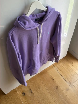 Lila hoodie från Polo Ralph Lauren - Snygg lila hoodie från Polo Ralph Lauren med klassisk huva och vita dragsnören. Har en känguruficka framtill och den ikoniska lilla loggan broderad på bröstet. Perfekt för en chill och avslappnad stil. Mvh ItsForfits 🌟