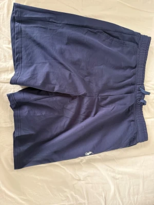 Marinblå shorts Polo Ralph Lauren - Snygga marinblå shorts  Polo Ralph Lauren med klassisk broderad logga i vitt på benet. Shortsen har elastisk midja med snörning och är tillverkade i mjuk bomull, perfekta för en avslappnad stil.