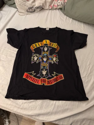 Guns N' Roses svart t-shirt - Säljer en svart t-shirt med stort Guns N' Roses Appetite for Destruction-tryck på framsidan. Klassisk rund hals och korta ärmar. Perfekt för dig som gillar rock och vill ha en ikonisk bandtröja i garderoben.