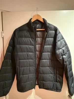 Abercrombie & Fitch dunjacka, storlek M - Snygg svart dunjacka från Abercrombie & Fitch med vattenavvisande material och quiltad design. Jackan har ståkrage, dragkedja framtill och två sidofickor. Sällan använd och i mycket bra skick.