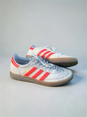 Adidas Spezial vita sneakers med röda ränder - Snygga Adidas Spezial sneakers i mockatyg med klassiska röda ränder på sidorna och guldfärgad logga. I fint skick. De har tyvärr blivit tvättade med tvål så mockan är hårdare än vanligt. Ställ gärna frågor.
