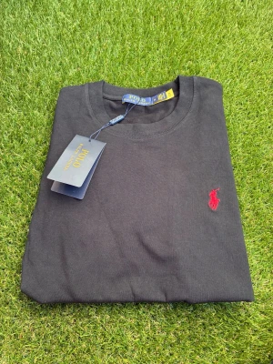 Svart t-shirt från Polo Ralph Lauren - Klassisk svart t-shirt från Polo Ralph Lauren med röd broderad logga på bröstet. T-shirten har rund halsringning och korta ärmar. Tillverkad i mjuk bomull för en skön känsla och enkel stil.
