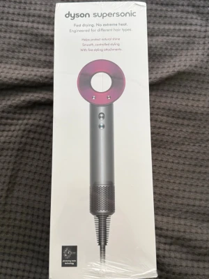 Dyson Supersonic hårfön med tillbehör - Säljer en Dyson Supersonic hårfön i silver och rosa. Medföljer fem stylingtillbehör: stylingkoncentrator, smoothing nozzle, diffuser, gentle air attachment och flyaway attachment. Modern design och avancerad teknologi för snabb torkning utan extrem värme.