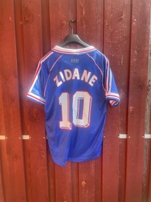 Frankrike Zidane VM 98 tröja Adidas - Klassisk blå fotbollströja från Adidas, Frankrikes landslag, VM 1998. Nummer 10 och Zidane på ryggen, vita och röda detaljer, Perfekt för dig som älskar retro och fotbollshistoria.