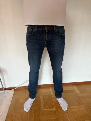 Mörkblå slim fit jeans från Nudie - Säljer ett par mörkblå slim fit jeans från Nudie Jeans med klassiska fem fickor och orangea sömmar. Jeansen har en smal passform och är tillverkade i denim med lätt stretch för extra komfort. Perfekta för en avslappnad och snygg stil. Modellen är Grim Tim. Hör av dig vid frågor mvh Ville