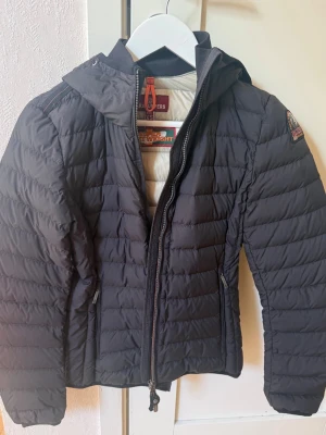 Svart pufferjacka från Parajumpers XS - Säljer en mörk blå tunn pufferjacka från Parajumpers i storlek XS. Jackan har huva, dragkedja framtill och två sidofickor med dragkedja. Klassisk patch på ärmen och lätt vadderad design som håller dig varm under kalla dagar. Använda cirka 10 gånger 