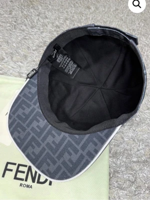 Svart keps med Fendi-logga - Snygg svart keps från Fendi med klassiskt FF-monogram över hela kepsen. Kepsen har böjd skärm och justerbar rem baktill. Tillverkad i bomullsmix och levereras med originalpåse och tagg. Perfekt för dig som gillar exklusiva accessoarer.
