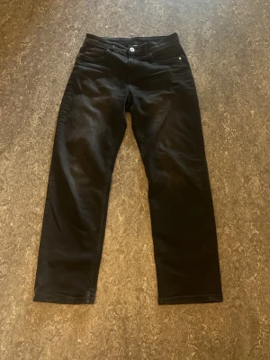 Svarta raka jeans - Svarta jeans med rak passform och klassisk femficksdesign. Jeansen har knapp och dragkedja framtill samt bälteshällor. Perfekta för en stilren och enkel look. Materialet ser ut att vara bomullsdenim med lite stretch. Vit färg på rumpan men med rätt tvätt så går de bort