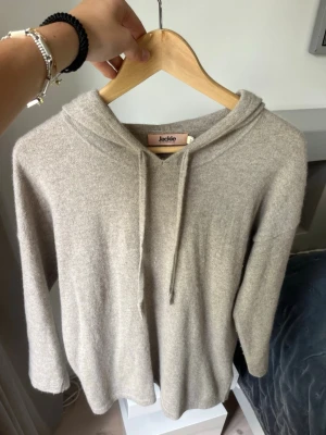 Beige hoodie från Jackie KASHMIR - Mysig beige hoodie från Jackie i mjukt stickat material. Hoodien har en klassisk huva med dragsko och avslappnad passform. Perfekt för dig som gillar en enkel och stilren look. Passar till det mesta och är superbekväm.